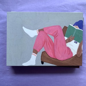 Pode incluir: Ilustração de uma pessoa relaxando em uma poltrona marrom, lendo um livro. A pessoa está usando calças rosa, uma camisa branca e meias brancas com a palavra "AMORE". O livro tem uma capa verde.