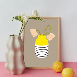 May include: A framed print of a yellow striped vase with three peach-coloured flowers. The vase is on a brown background. The print is on a table with a white vase and two lemons.