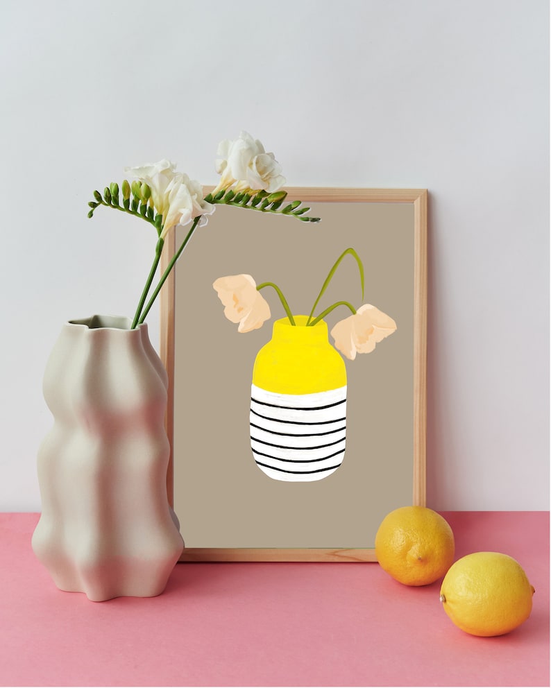May include: A framed print of a yellow striped vase with three peach-coloured flowers. The vase is on a brown background. The print is on a table with a white vase and two lemons.