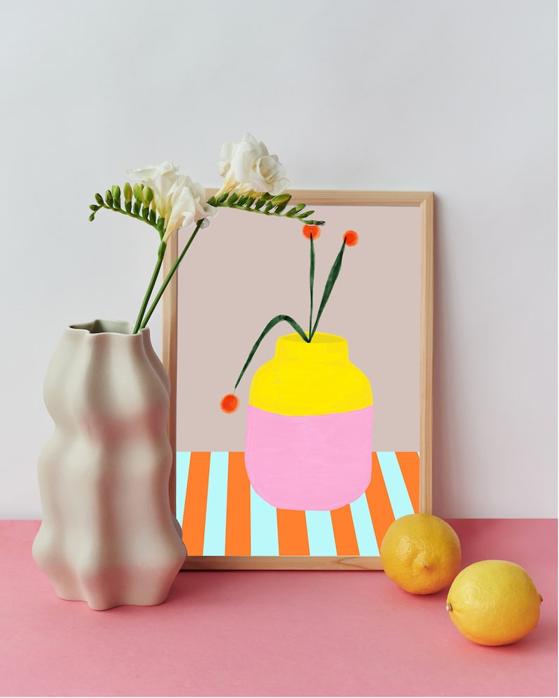 Pode incluir: Uma impress&atilde;o emoldurada de um vaso amarelo e rosa com caules verdes e flores laranja sobre um fundo listrado. O vaso est&aacute; sobre uma mesa com duas limas.