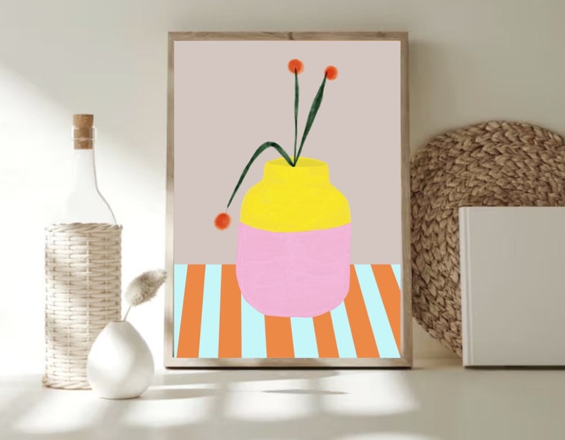 Pode incluir: Um vaso amarelo e rosa com um caule verde e tr&ecirc;s flores laranja sobre um fundo listrado.