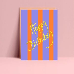 Könnte beinhalten: Eine Grußkarte mit Holzrahmen. Die Karte hat orangefarbene und blauviolette vertikale Streifen. Die Worte "Happy Birthday" sind in gelber Schrift auf die Vorderseite geschrieben.