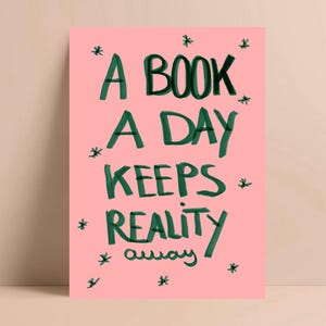 Pu&ograve; includere: Una stampa artistica rosa con il testo scritto a mano in verde scuro "A BOOK A DAY KEEPS REALITY away". Piccole forme di stella verde scuro sono sparse intorno al testo. La stampa ha un design minimalista.