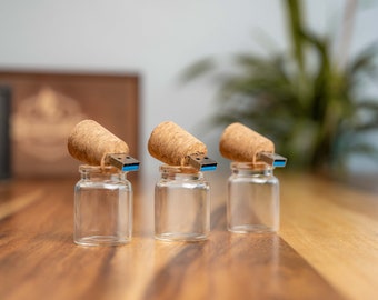 May include: Three small glass jars with cork tops and USB drives inserted into the cork. The jars are sitting on a wooden surface.