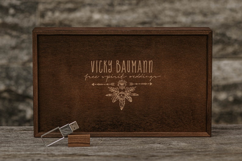 May include: A wooden box containing a USB drive and a small wooden block. The box is engraved with the text "Vicky Baumann Free Spirit Weddings" and a stylised design of feathers, an eye, and arrows.