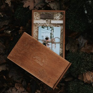 May include: A wooden box with a photo of a couple inside. The box is engraved with the words "Jana Maria" and has a rustic brown finish.