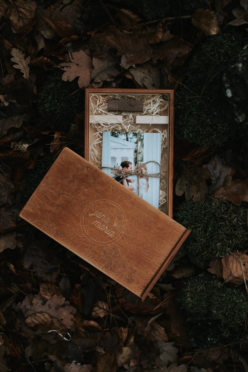 May include: A wooden box with a photo of a couple inside. The box is engraved with the words "Jana Maria" and has a rustic brown finish.