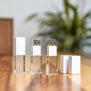 Könnte beinhalten: Vier weiße USB-Sticks mit silbernen Metallsteckern. Die Sticks sind in einer Reihe auf einer Holzoberfläche angeordnet.