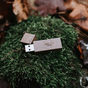 May include: A wooden USB flash drive with a personalized inscription that reads "Jana Maria" in a circle. The drive is sitting on a bed of green moss.