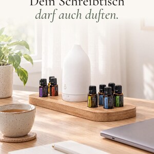Könnte beinhalten: Ein weißer Keramik-Diffusor für ätherische Öle und mehrere kleine dunkle Glasfläschchen auf einem rechteckigen Holztablett. Der Text lautet: HOMEOFFICE, ABER SCHÖN. Dein Schreibtisch darf auch duften.