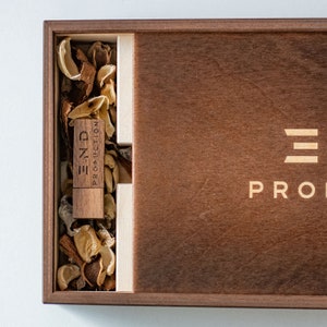 May include: A wooden box with a USB drive inside. The USB drive is labeled "END PRODUCTION". The box is made of dark wood and has a light wood inlay. The box is closed and the lid is slightly ajar.