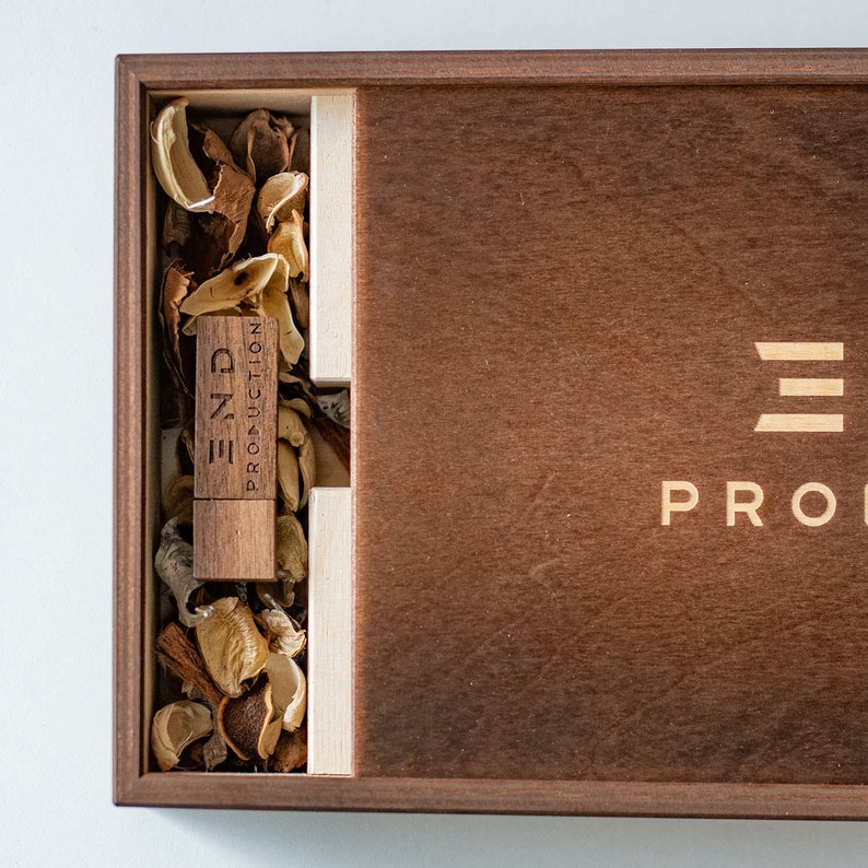 May include: A wooden box with a USB drive inside. The USB drive is labeled "END PRODUCTION". The box is made of dark wood and has a light wood inlay. The box is closed and the lid is slightly ajar.