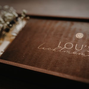 May include: A dark brown wooden box with a light brown inscription that reads "LOU'S moments" with a small heart symbol above the text.