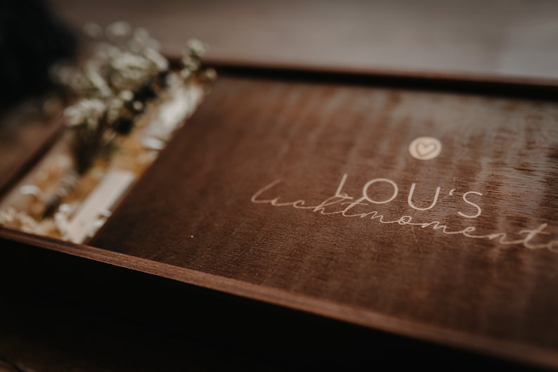 May include: A dark brown wooden box with a light brown inscription that reads "LOU'S moments" with a small heart symbol above the text.