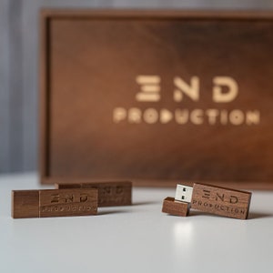 May include: Four wooden USB flash drives with the text "END PRODUCTION" engraved on them. The flash drives are on a white surface in front of a wooden box with the same text engraved on it.