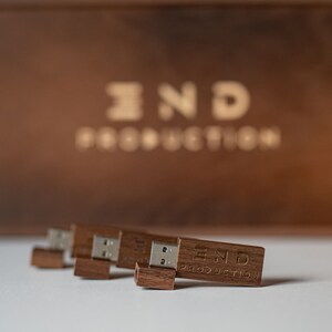 May include: Four wooden USB drives with the text "END PRODUCTION" engraved on the front. The drives are arranged in a row on a white surface.