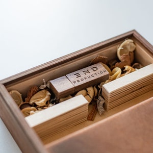 May include: A wooden box with a wooden USB drive inside. The USB drive is engraved with the text "END PRODUCTION". The box is filled with wood shavings.