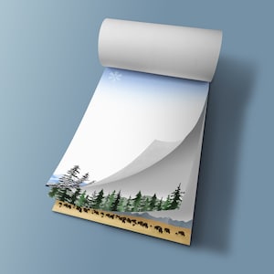 May include: A notepad with a winter landscape design. The pages feature a watercolor illustration of a forest, mountains, and a herd of bison. The top page has a snowflake and a gradient blue sky.