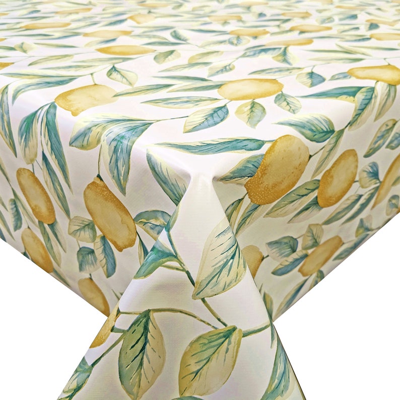 May include: White tablecloth with a lemon and leaf pattern. The lemons are yellow and the leaves are green.