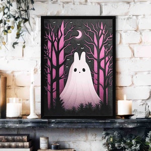 May include: A black framed print with a pink and black illustration of a ghost in a forest. The ghost is white with a pink gradient and has a crescent moon above it.