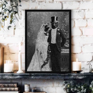 May include: A black and white photograph of a couple dressed in wedding attire. The groom is wearing a top hat and a tuxedo. The bride is wearing a white dress and veil. The photo is framed in a black frame.