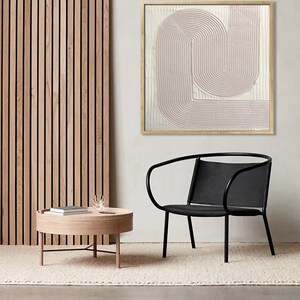 Peut inclure: Une chaise noire avec un dossier incurv&eacute; et une table basse en bois clair avec un plateau rond. Un tableau abstrait encadr&eacute; avec un motif rose et blanc est accroch&eacute; au mur derri&egrave;re la chaise.