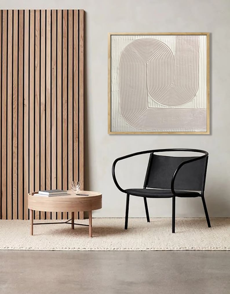 Peut inclure: Une chaise noire avec un dossier incurv&eacute; et une table basse en bois clair avec un plateau rond. Un tableau abstrait encadr&eacute; avec un motif rose et blanc est accroch&eacute; au mur derri&egrave;re la chaise.