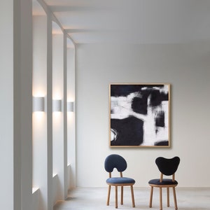 May include: Two chairs with a unique, organic shape and wooden legs. The chairs are upholstered in dark blue and black fabric. A black and white abstract painting hangs on the wall behind the chairs.