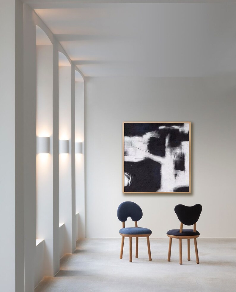 May include: Two chairs with a unique, organic shape and wooden legs. The chairs are upholstered in dark blue and black fabric. A black and white abstract painting hangs on the wall behind the chairs.