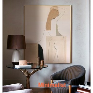 May include: Abstract art print featuring a nude figure in shades of brown, beige, and green. The print is framed in a gold frame and hangs on a wall in a living room setting.