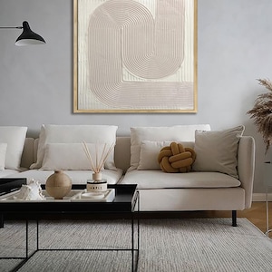 Peut inclure: Une peinture abstraite rose p&acirc;le avec un design textur&eacute; et superpos&eacute;. La peinture est encadr&eacute;e dans un cadre en bois naturel et est accroch&eacute;e &agrave; un mur gris clair au-dessus d'un canap&eacute; blanc.