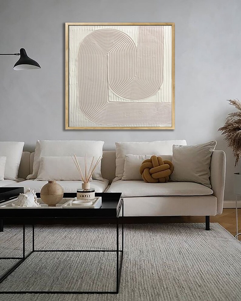 Peut inclure: Une peinture abstraite rose p&acirc;le avec un design textur&eacute; et superpos&eacute;. La peinture est encadr&eacute;e dans un cadre en bois naturel et est accroch&eacute;e &agrave; un mur gris clair au-dessus d'un canap&eacute; blanc.