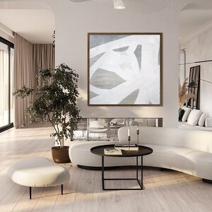 May include: Abstract painting with white lines on a gray background. The painting is framed in a light wood frame and is hanging on a white wall in a modern living room.