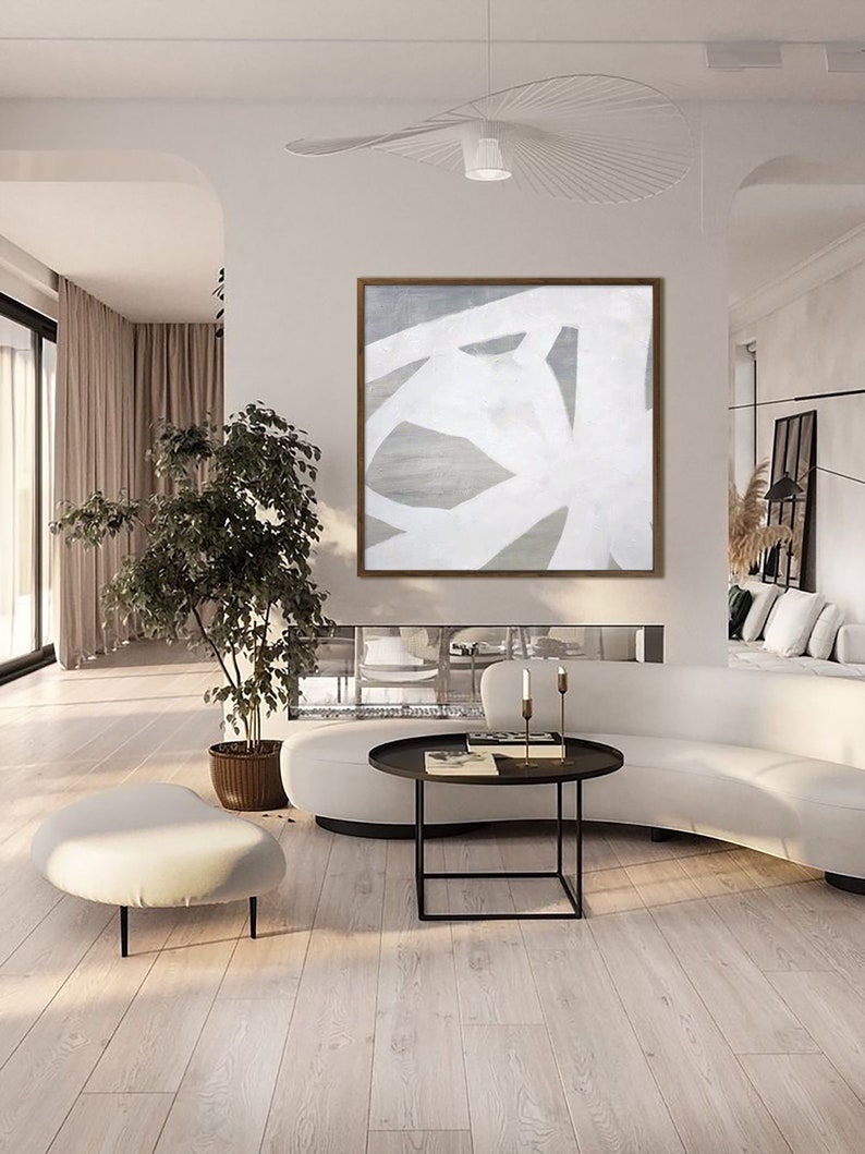 May include: Abstract painting with white lines on a gray background. The painting is framed in a light wood frame and is hanging on a white wall in a modern living room.