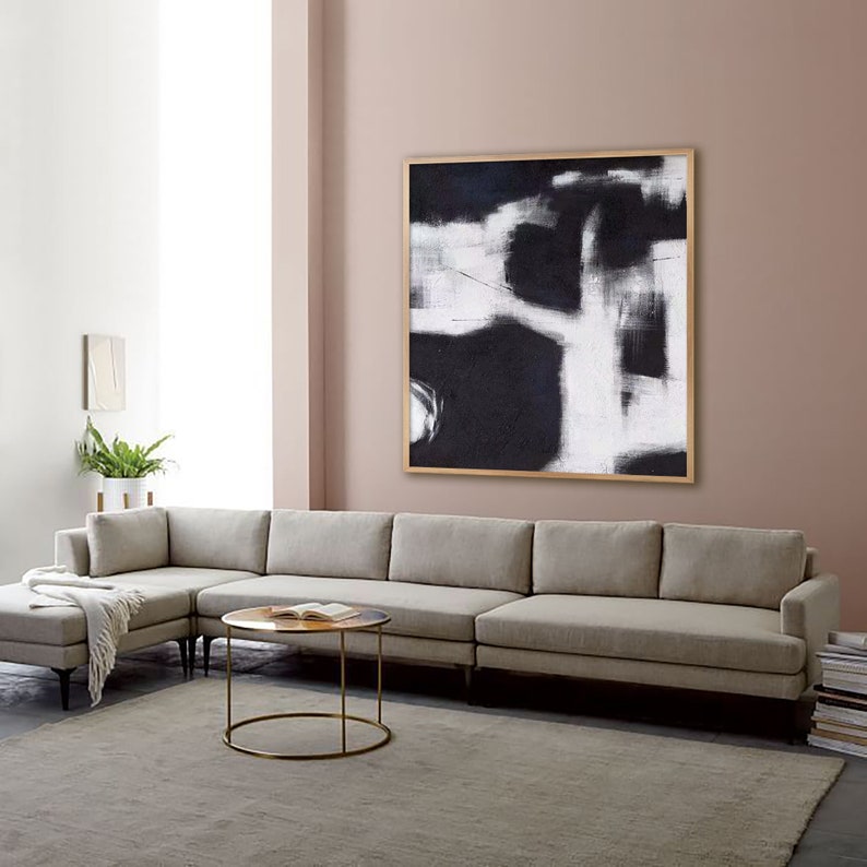 May include: A large, square, black and white abstract painting with a wooden frame hangs on a light pink wall above a light gray sectional sofa.