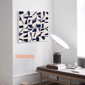 May include: A minimalist painting with a white background and geometric shapes in navy blue. The painting is hanging on a white wall in a room with a lamp and a bench.