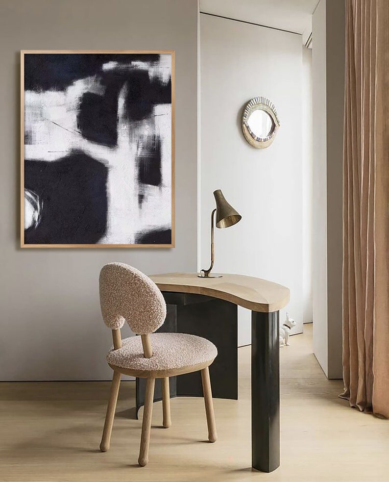 May include: A black and white abstract painting hangs above a wooden desk with a curved top. A fluffy white chair sits in front of the desk. A gold lamp with a white shade sits on the desk.