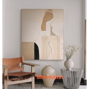 May include: Abstract art print of a nude figure in shades of brown, beige, and green. The print is framed and hanging on a white wall above a brown leather chair and a silver side table.