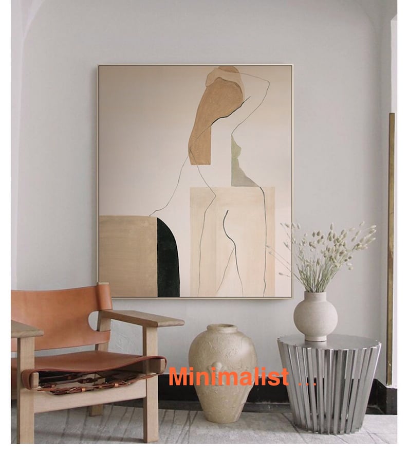 May include: Abstract art print of a nude figure in shades of brown, beige, and green. The print is framed and hanging on a white wall above a brown leather chair and a silver side table.
