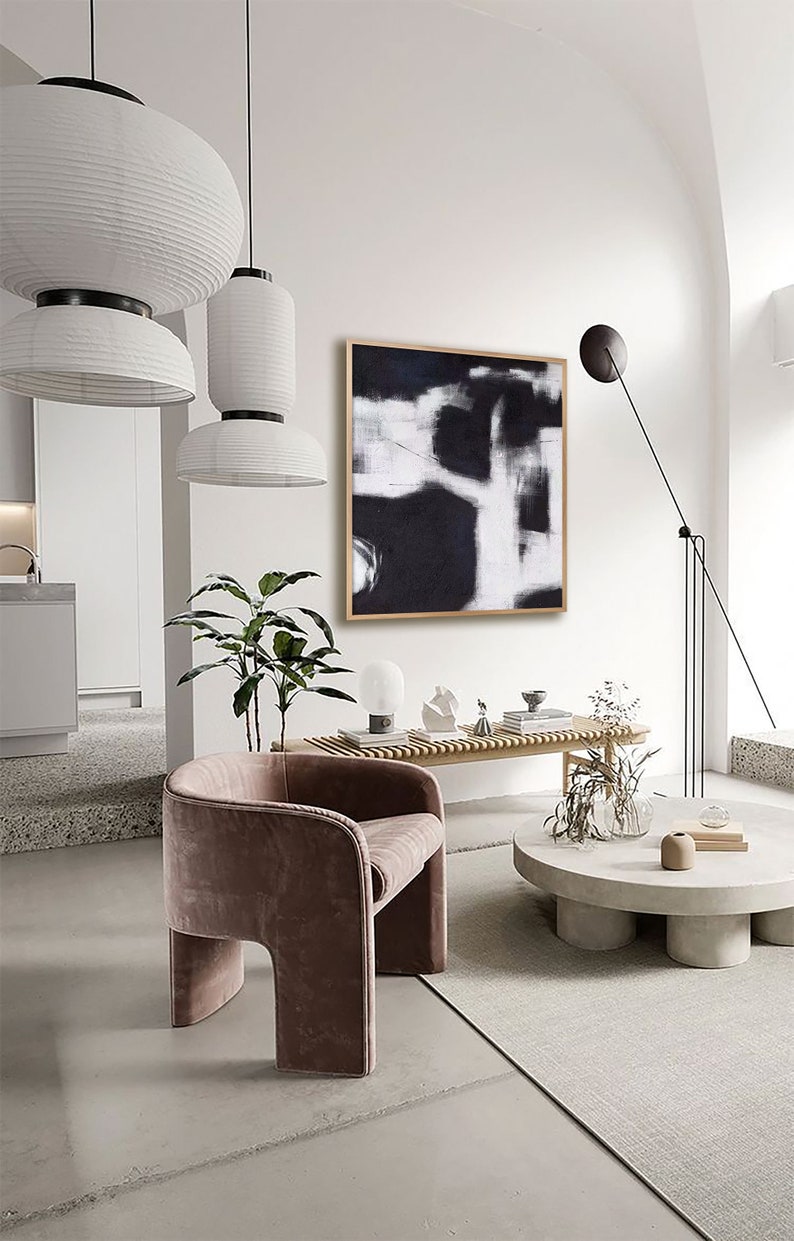 May include: A modern living room interior with a black and white abstract painting hanging on a white wall. A brown velvet armchair sits in front of a concrete coffee table with a vase of dried flowers.