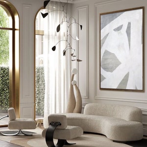 May include: A living room interior with a white, curved sofa, two white chairs with black metal bases, a white and gray abstract painting, and a black mobile hanging from the ceiling.