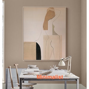 May include: Abstract art print featuring a nude figure in shades of beige, brown, and green. The print is framed and hanging on a light brown wall above a desk with a lamp and two chairs.
