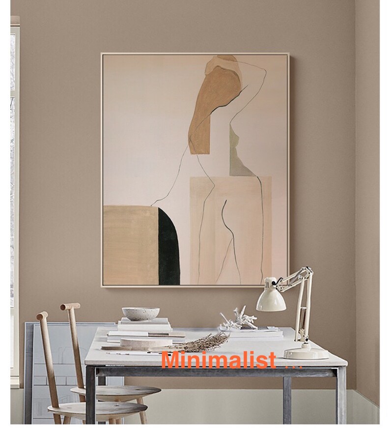May include: Abstract art print featuring a nude figure in shades of beige, brown, and green. The print is framed and hanging on a light brown wall above a desk with a lamp and two chairs.
