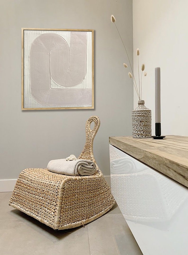 Peut inclure: Une chaise ber&ccedil;ante en osier tress&eacute; avec une finition brun clair. La chaise est pos&eacute;e sur un sol en carrelage brun clair. Une serviette blanche est pli&eacute;e sur l'assise de la chaise. Un meuble blanc avec un dessus en bois se trouve en arri&egrave;re-plan. Un vase avec des fleurs s&eacute;ch&eacute;es et une bougie sont sur le meuble.