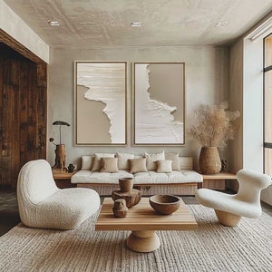 Op de afbeelding: Twee abstracte beige en witte textuur canvas schilderijen met houten frames hangen aan een muur boven een witte bank met beige kussens. De bank staat in een woonkamer met een houten salontafel, een wit tapijt en een witte stoel.
