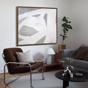 May include: A brown velvet armchair with a white and brown patterned pillow sits in a living room with a black coffee table and a white lamp. A framed abstract painting with white and gray lines hangs on the wall behind the chair.