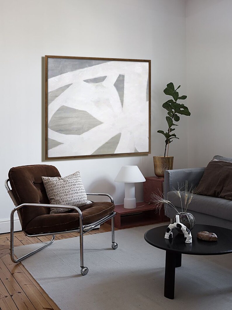 May include: A brown velvet armchair with a white and brown patterned pillow sits in a living room with a black coffee table and a white lamp. A framed abstract painting with white and gray lines hangs on the wall behind the chair.