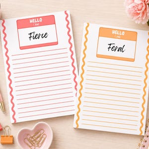 Op de afbeelding: Twee rechthoekige notitieblokken met golvende randen. Het linkerblok heeft een roze rand en een label met de tekst "HELLO I AM Fierce". Het rechterblok heeft een oranje rand en een label met "HELLO I AM Feral". Beide hebben horizontale lijnen.