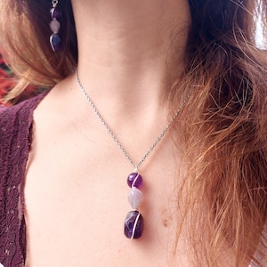 May include: A silver chain necklace with a pendant featuring three amethyst stones of varying sizes and shades of purple.