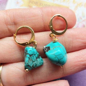 May include: A pair of gold hoop earrings with turquoise gemstone drops. The turquoise stones are a mottled blue-green color.